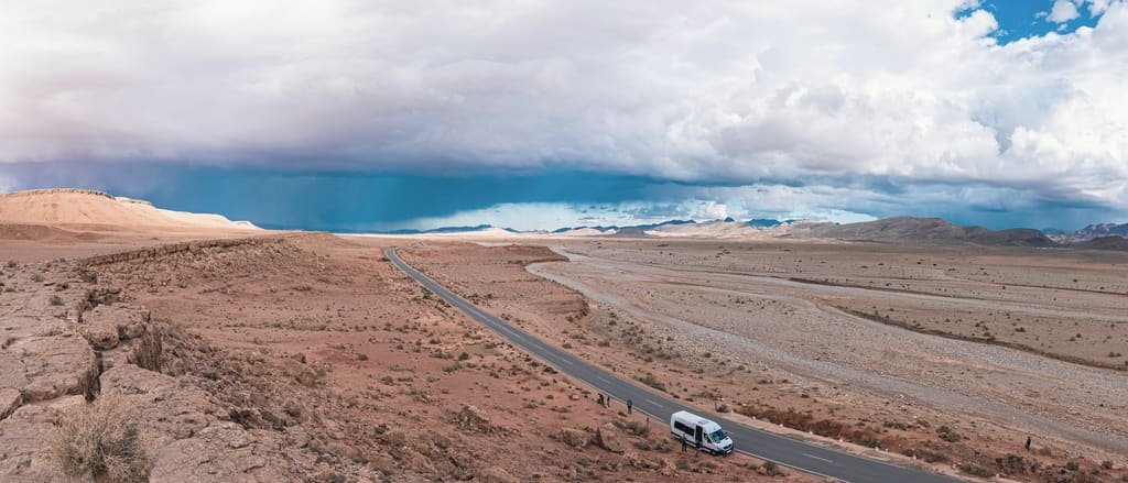 A delivery van on a long highway crossing the desert under a wide sky