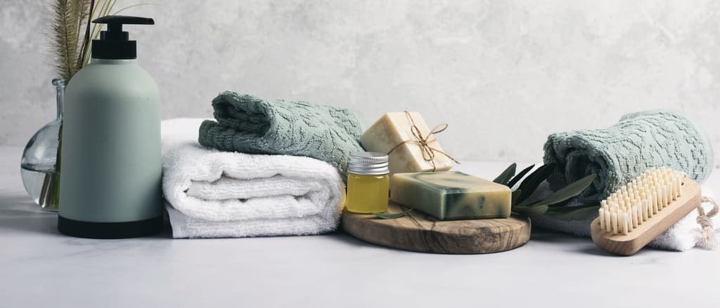 A soap dispenser, folded towels, soap bars and a bath brush