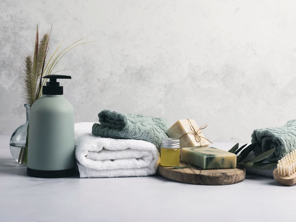 A soap dispenser, folded towels, soap bars and a bath brush