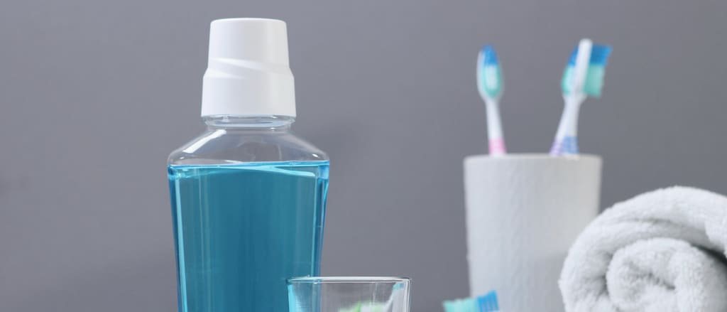 A bottle of mouthwash, a glass and toothbrushes beside a folded towel