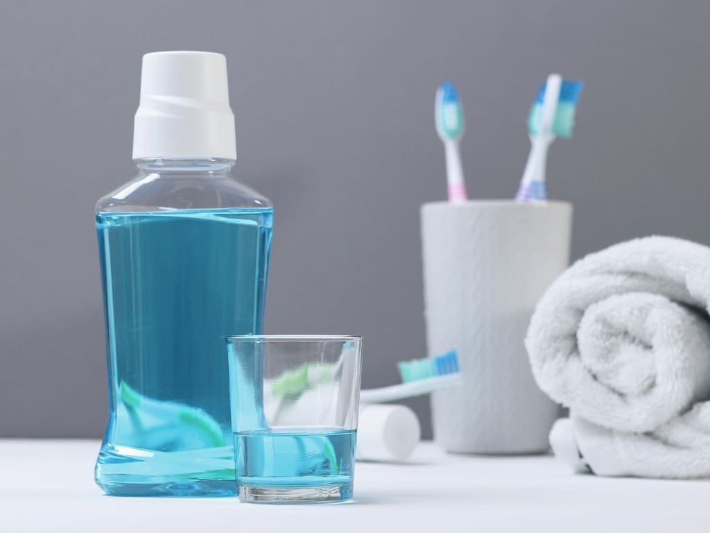 A bottle of mouthwash, a glass and toothbrushes beside a folded towel