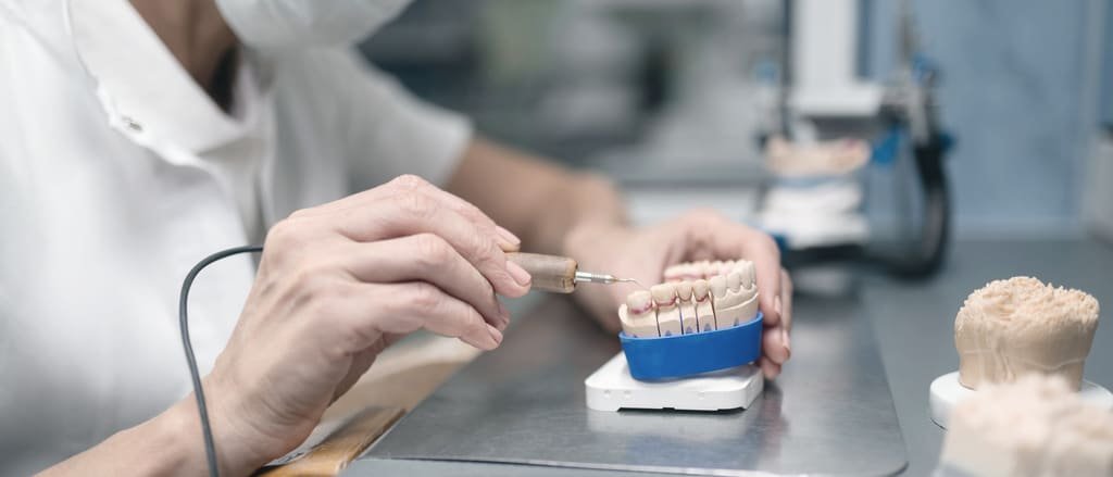 A dental technician finishing a set of prosthetic teeth at the laboratory bench