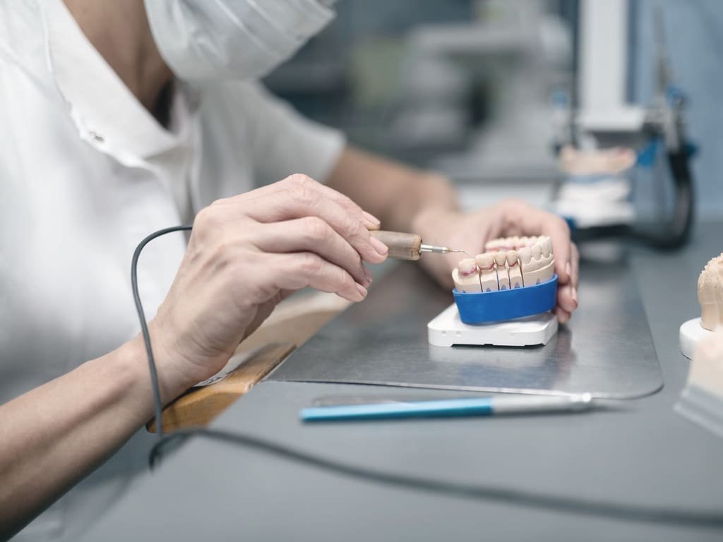 A dental technician finishing a set of prosthetic teeth at the laboratory bench