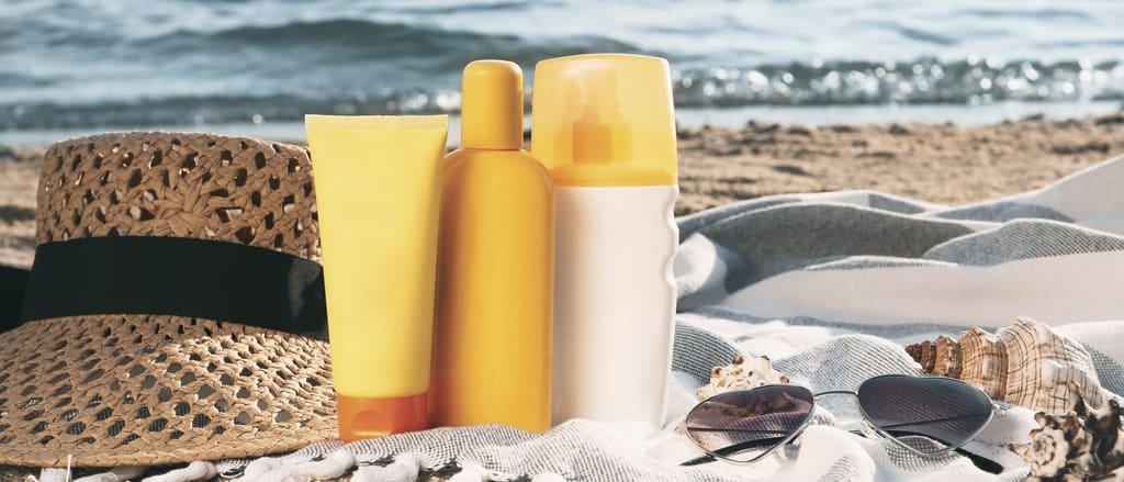 Sun protection products, a straw hat and sunglasses on a beach blanket by the sea