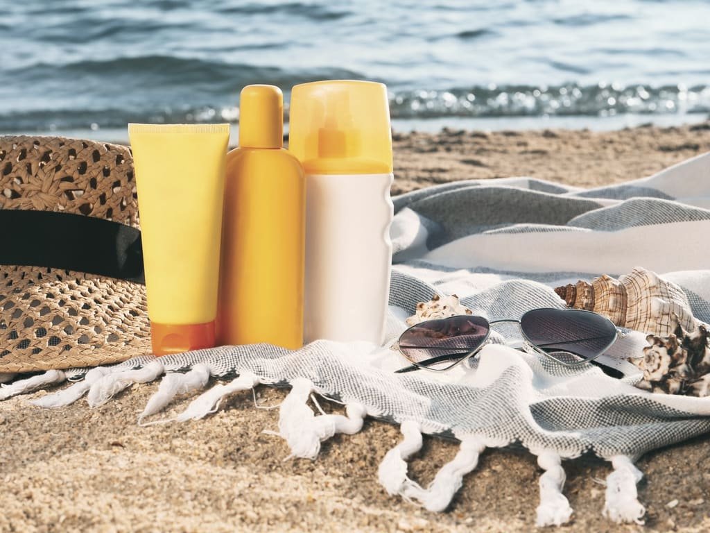 Sun protection products, a straw hat and sunglasses on a beach blanket by the sea