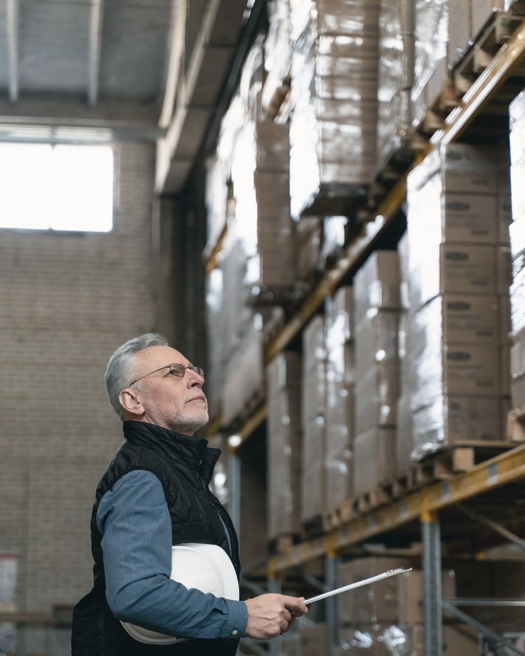 A warehouse manager checking stock on a tablet between tall racks of boxed goods