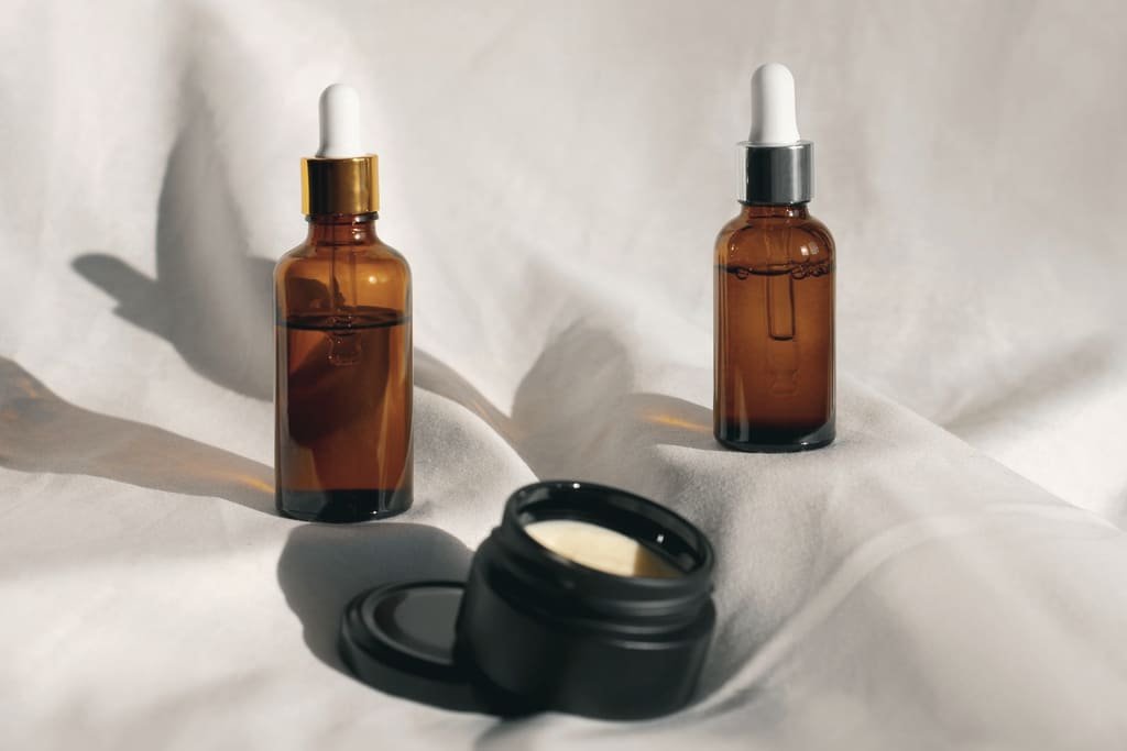 Amber serum dropper bottles and an open jar of cream on white linen