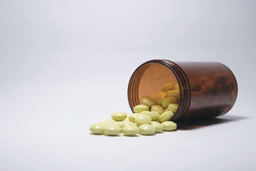 An amber bottle of tablets spilling onto a white surface